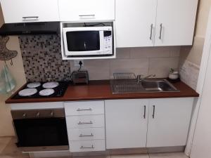 a kitchen with white cabinets and a microwave and a sink at Little Tree Loft in Uitenhage