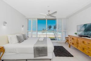 a white bedroom with a bed and a tv at Golden Sands on the Beach - Absolute Beachfront Apartments in Gold Coast