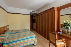 Un dormitorio con una cama y un escritorio con un jarrón de flores en Sporthotel Olimpo, en Garda