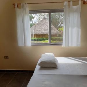 a bed with a pillow in front of a window at Bushbaby Lodge in Mukono