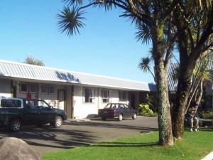 samochód zaparkowany przed budynkiem z palmą w obiekcie Greymouth Kiwi Holiday Park & Motels w mieście Greymouth