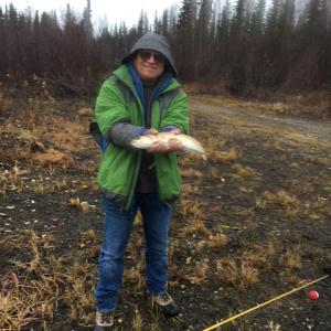 a woman holding a fish in a field at Alaska Log Cabins on the Pond in Clear Creek Park