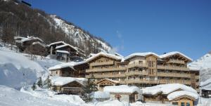 un grand bâtiment recouvert de neige devant une montagne dans l'établissement Hôtel Les Barmes De l'Ours, à Val dʼIsère