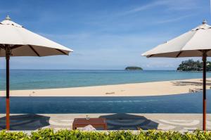 a beach with two umbrellas and the ocean at The Shore At Katathani - Adult Only - SHA Extra Plus in Kata Beach