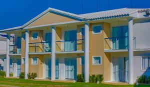 żółty budynek z białymi kolumnami i niebieskimi oknami w obiekcie Residencial Mar da Galilei - Apartamento 20A w mieście Porto Seguro