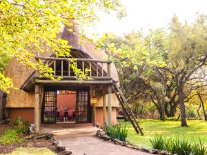 a thatch roofed house with a porch and a ladder at aha Lesedi African Lodge & Cultural Village in Pelindaba