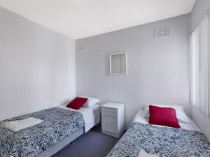 two beds in a room with white walls and red pillows at Dolphin Court 6 in The Entrance