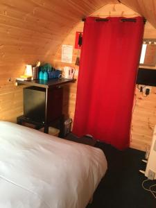 Cette chambre comprend un lit et un rideau rouge. dans l'établissement Poplars Farm Site Glamping Pods, à Hulland