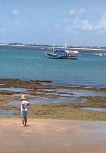 village na praia do forte في برايا دو فورتي: شخص يمشي على الشاطئ مع قارب في الماء