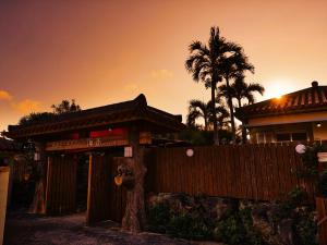 a building with a fence and a palm tree at Nagahama Beach Resort Kanon in Nakijin