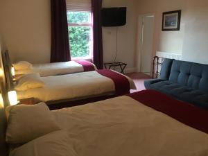 Habitación de hotel con 3 camas y sofá azul en Holly Trees Hotel en Alsager