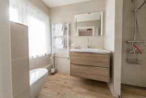een badkamer met een wastafel, een bad en een spiegel bij Hotel-Restaurant de Boer'nkinkel in Hoenderloo