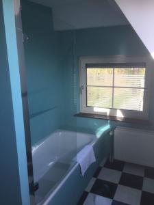 ein blaues Bad mit einer Badewanne und einem Fenster in der Unterkunft B&B de Druif in Breda