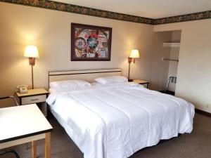 コロラドスプリングスにあるTravelStar Inn & Suitesの白い大型ベッド1台とテーブル2台が備わるホテルルームです。