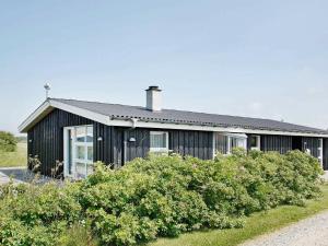 ロッケンにあるThree-Bedroom Holiday home in Løkken 54の白い扉と茂みのある黒い家