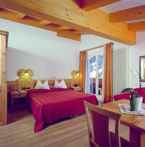 1 dormitorio con cama roja y mesa en Hotel Alba Wellness & Spa, en Canazei