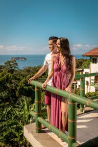 a man and a woman standing on a railing with the ocean in the background at Si Como No Resort & Wildlife Refuge in Manuel Antonio