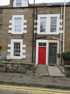 a brick house with a red door on a street at WEE NEUK in Cellardyke