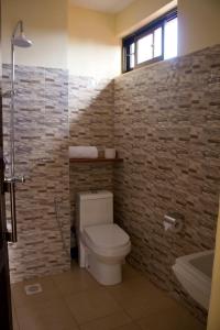 a bathroom with a toilet and a brick wall at Lilac Elevate Inn in Karatu