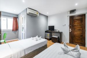 two beds in a room with a tv and a desk at The Richy Place Guest House in Bangkok