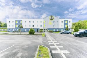 een groot wit gebouw met auto's geparkeerd op een parkeerplaats bij B&B HOTEL Freyming-Merlebach in Freyming