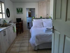 a bedroom with a bed with white sheets and a kitchen at Rustverseker Self Catering Accommodation in George