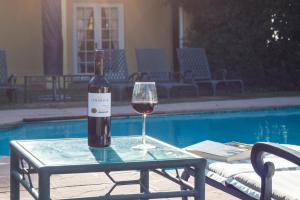 una botella de vino y una copa en una mesa junto a la piscina en Lyngrove Wines & Guesthouse, en Stellenbosch