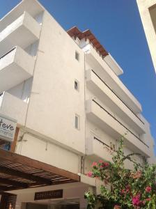 un edificio blanco alto con un árbol delante de él en Aialion studios & apartments - Steve Apartments, en Rodas
