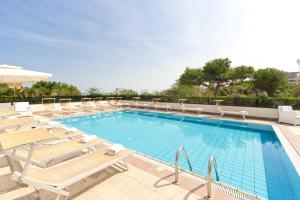 una gran piscina con tumbonas y mesas. en Hotel Parco, en Riccione