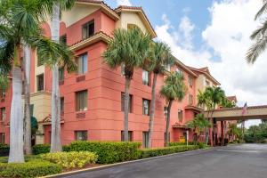 パームビーチ・ガーデンズにあるBest Western Plus Palm Beach Gardens Hotel & Suites and Conference Ctのヤシの木が目の前に広がるピンクの建物