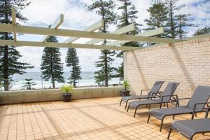 a patio with chairs and a brick wall and the ocean at Beachfront Manly Apartment With Balcony & Parking DUPLICATE in Sydney