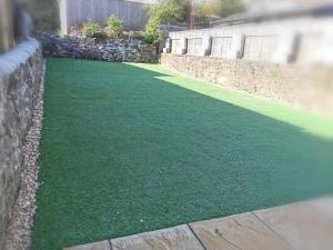 a artificial lawn in a yard next to a stone wall at Spacious 4BR Home with Garden, Swansea in Swansea