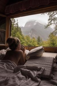 Una mujer acostada en la cama mirando por la ventana en Cottage Trenta, en Bovec