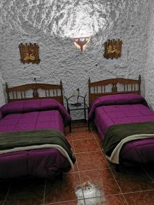 GraenaにあるCuevas La Solanaの紫のシーツが備わる客室内のベッド2台