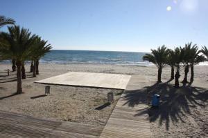 einen Sandstrand mit Palmen und einer hölzernen Promenade in der Unterkunft Fantástico apartamento con piscina in Santa Pola