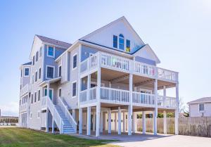 a large house with stairs in front of a fence at By the Sea in Kill Devil Hills