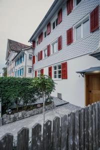 a white building with red windows and a wooden fence at Clara Erdgeschosswohnung im Jüdischen Viertel in Hohenems