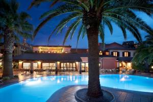 a pool with palm trees in front of a hotel at Hotel Corallaro in Santa Teresa Gallura