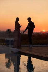 a man and woman standing next to a pool at sunset at 18 Grapes Hotel in Agios Prokopios