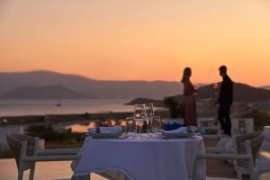 a table with wine glasses and a couple standing on a balcony at 18 Grapes Hotel in Agios Prokopios