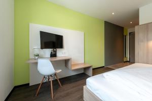 a bedroom with a bed and a tv and a chair at a2 HOTELS Denkendorf - Airport & Messe in Denkendorf