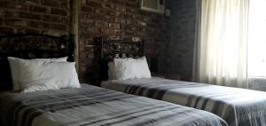 2 camas en un dormitorio con una pared de ladrillo en Klein Plasie Lodge, en Hartswater