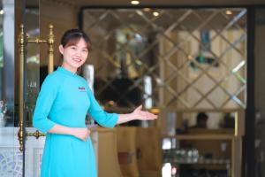 a woman in a blue dress standing with her hand outstretched at Le Beryl Hanoi Hotel in Hanoi