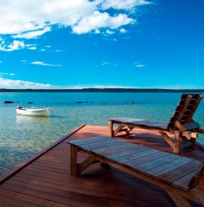 Eumarella Shores Noosa Lake Retreat في نوسافيل: مقعد على رصيف مع قارب في الماء