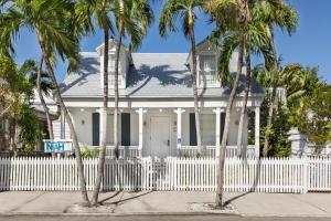 a white fence in front of a white house with palm trees at Nyah - Adult Exclusive in Key West