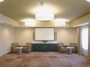 Candlewood Suites Fort Collins, an IHG Hotel في فورت كولينز: غرفة كبيرة فيها شاشة وكراسي وغرفة كبيرة فيها شاشة كبيرة