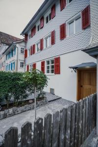 a house with red shuttered windows and a wooden fence at MINA Stadtwohnung im Jüdischen Viertel in Hohenems