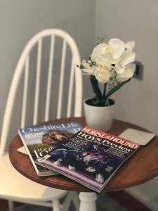 una mesa con una revista y un jarrón con flores blancas en The Loft en Congleton