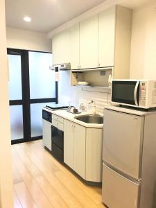 eine weiße Küche mit einer Spüle und einer Mikrowelle in der Unterkunft Motomachi Flat in Fukuyama