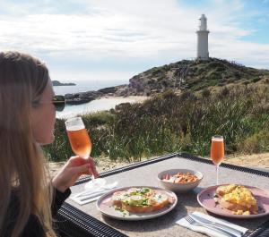 a woman sitting at a table with food and a lighthouse at Discovery Rottnest Island in Rottnest Island
